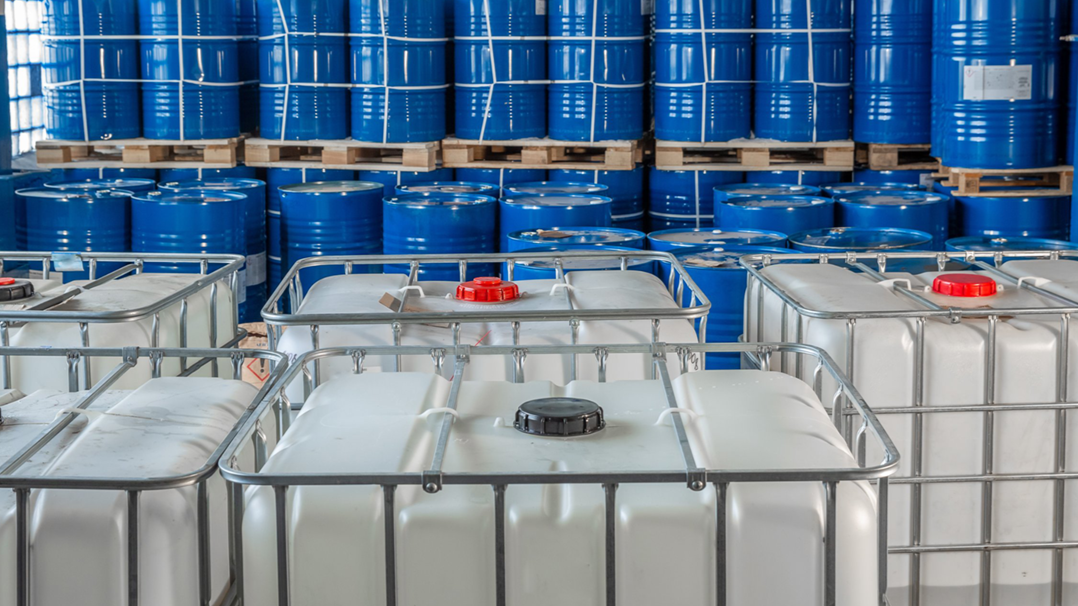 Storage area with blue barrels on pallets and white plastic containers.